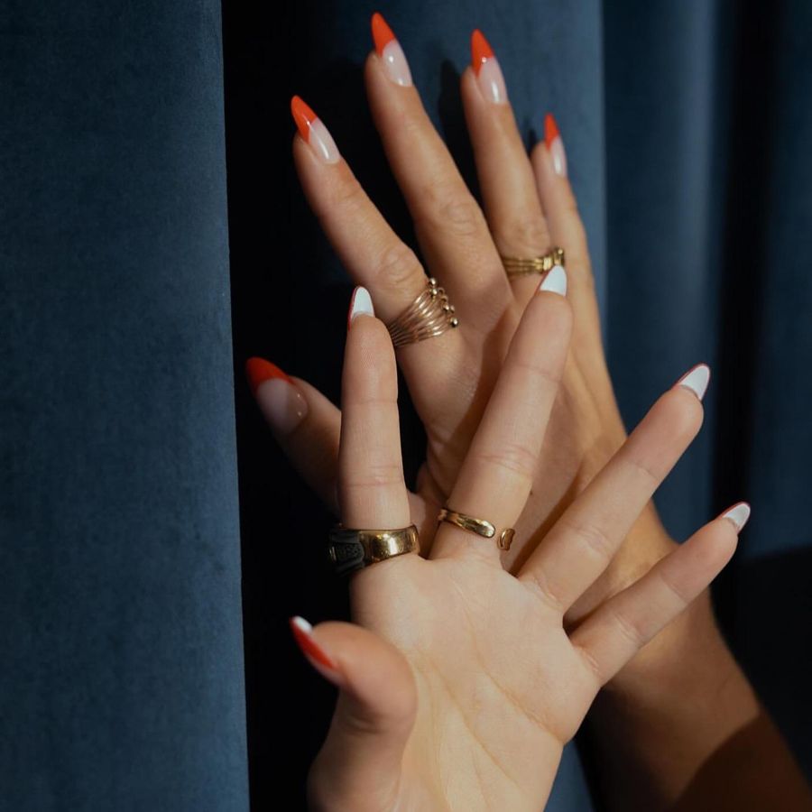 Hand detail: red-orange tipped nails and gold rings against blue velvet