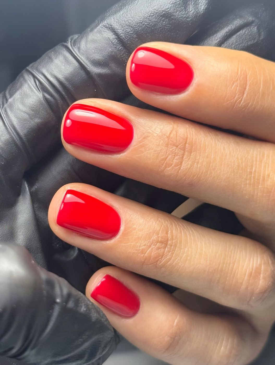 Short natural nails in a glossy classic red, held in a gloved hand